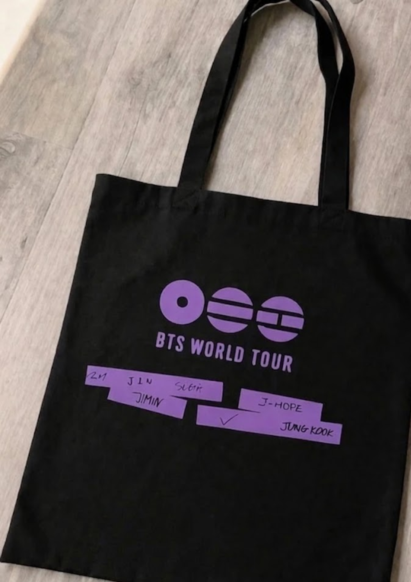 Black tote bag with purple 'BTS World Tour' Fanmade Kpop text on a wooden surface
